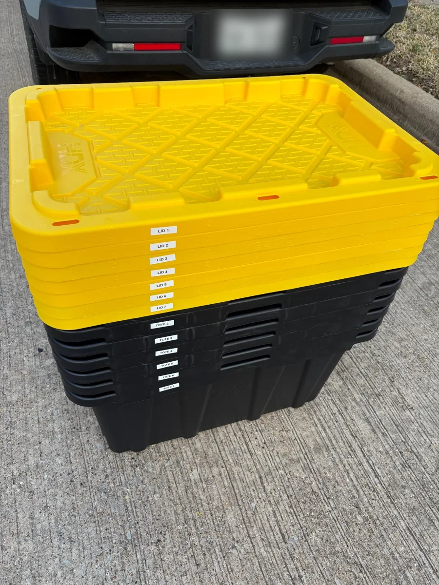 Nested black moving totes and stacked yellow lids behind a parked SUV