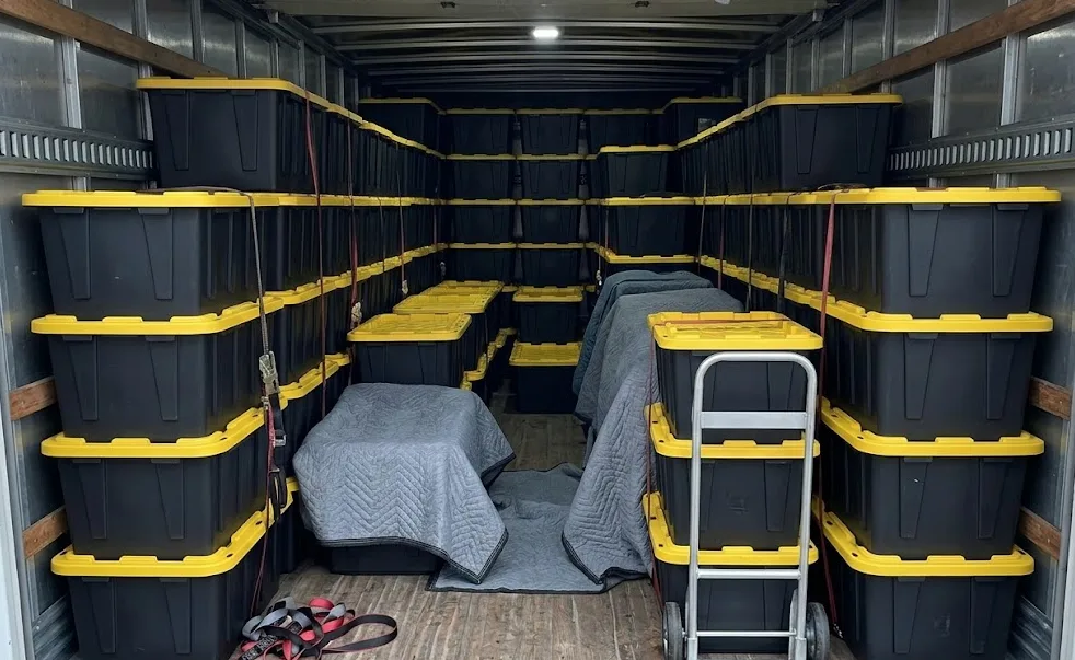 Black moving totes with yellow lids stacked inside a trailer